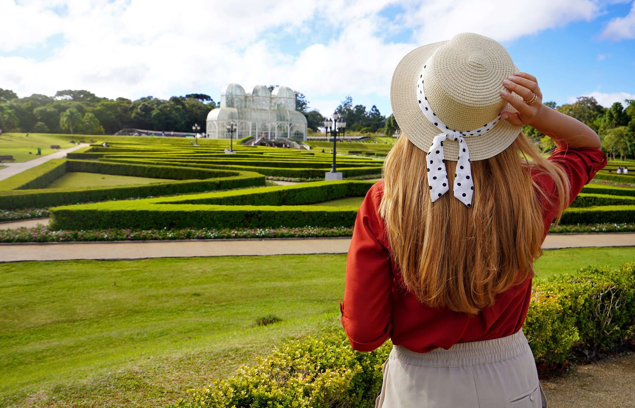 Femme avec un chapeau admirant le Jardin Botanique de Curitiba, Brésil, entourée de gazon et de végétation