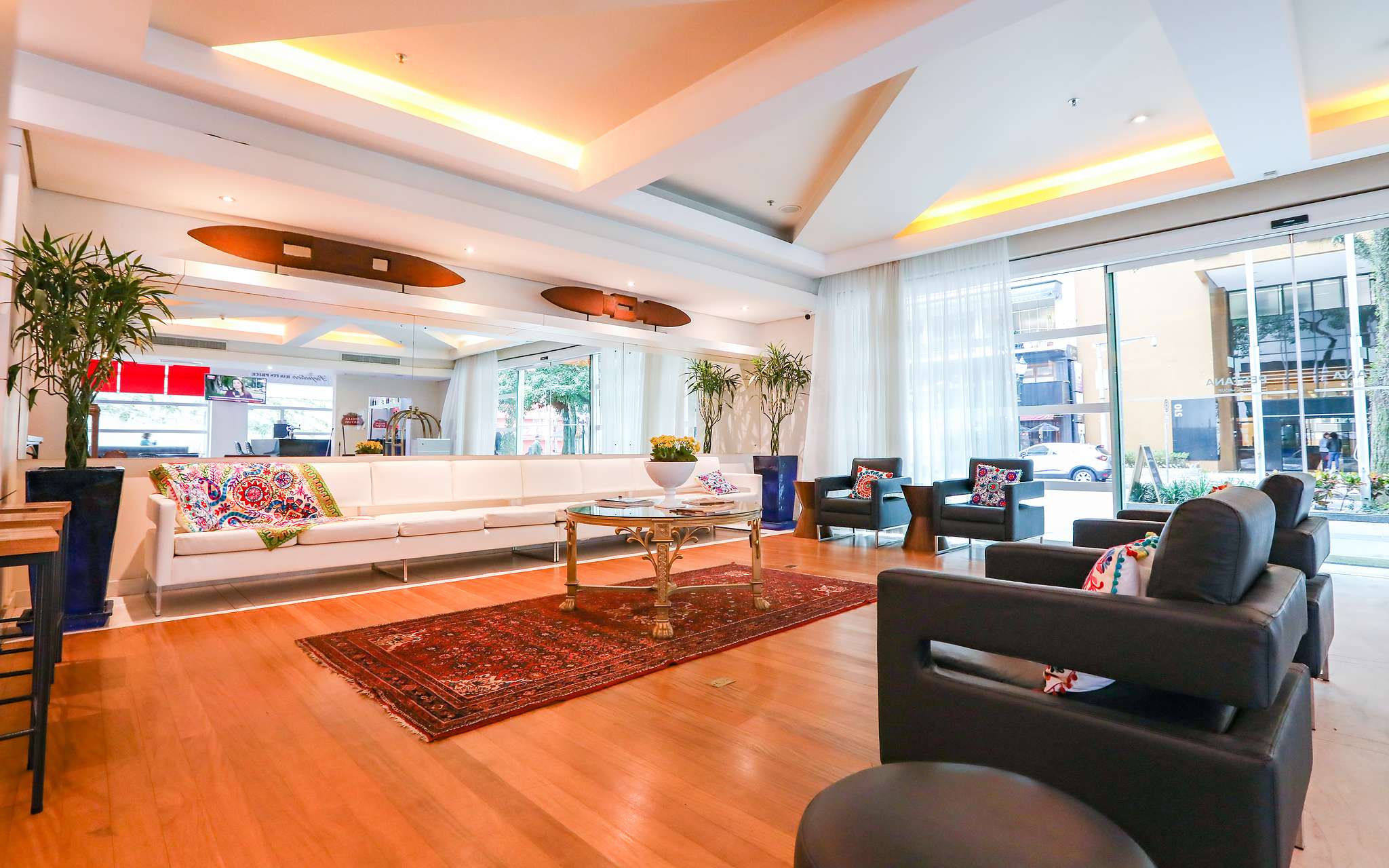 Entrée du Pestana Curitiba avec 4 fauteuils et un long canapé blanc avec des coussins colorés et une table basse