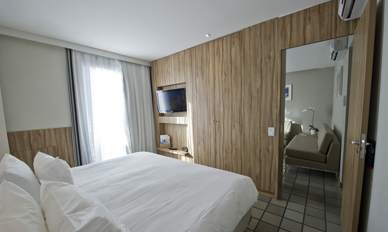 La Suite Standard du Pestana Rio Atlântica a une chambre avec lit double et télévision, et un salon avec canapés et climatisation