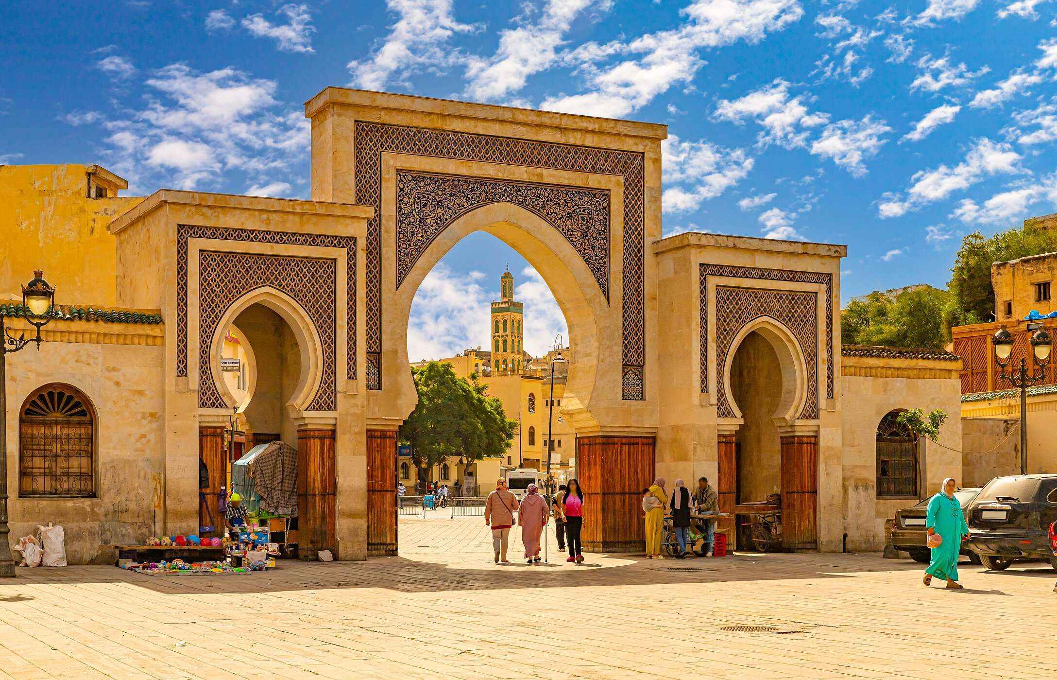Arches typiques marocains à Fès, avec des carreaux couleur sable et des gens en habits traditionnels.