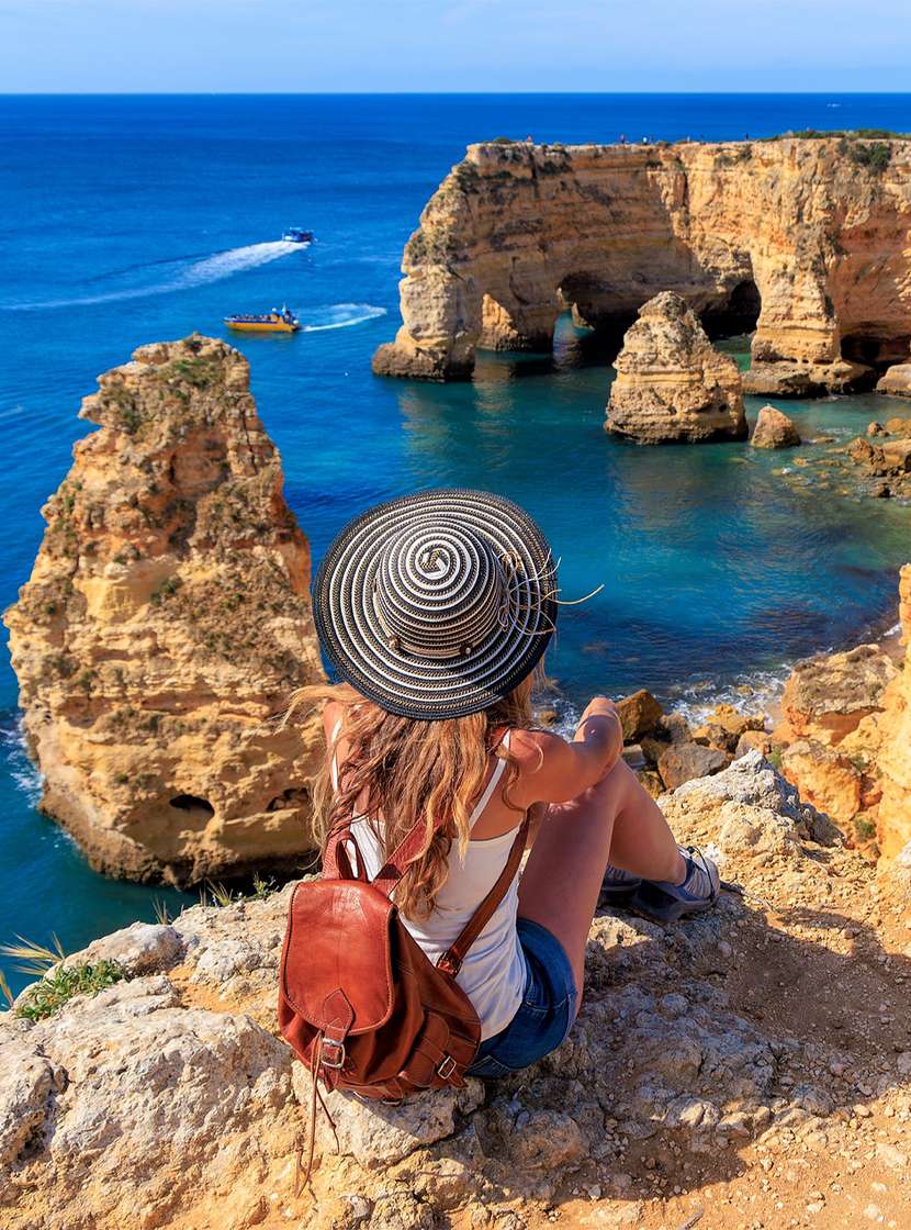 Femme admirant la vue panoramique de la côte de l'Algarve, avec des eaux cristallines et une falaise entourée de végétation