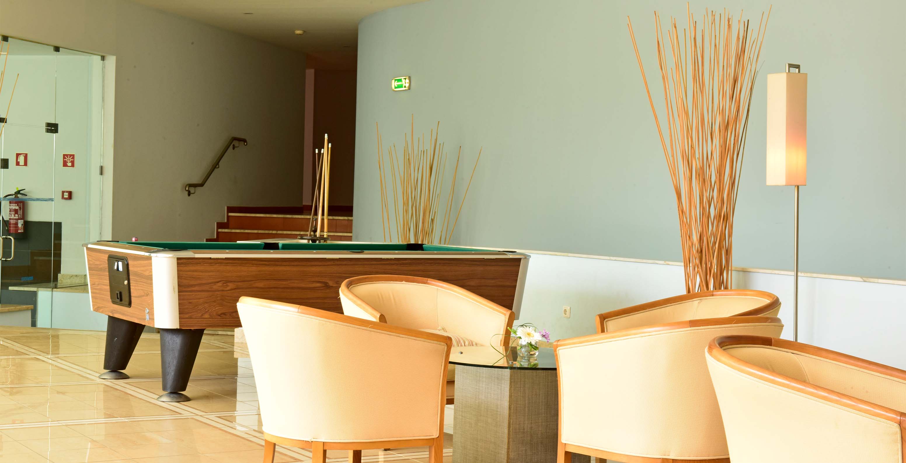 Salle de jeux avec table de billard, chaises et table d'appoint centrale, avec escaliers au fond et décoration