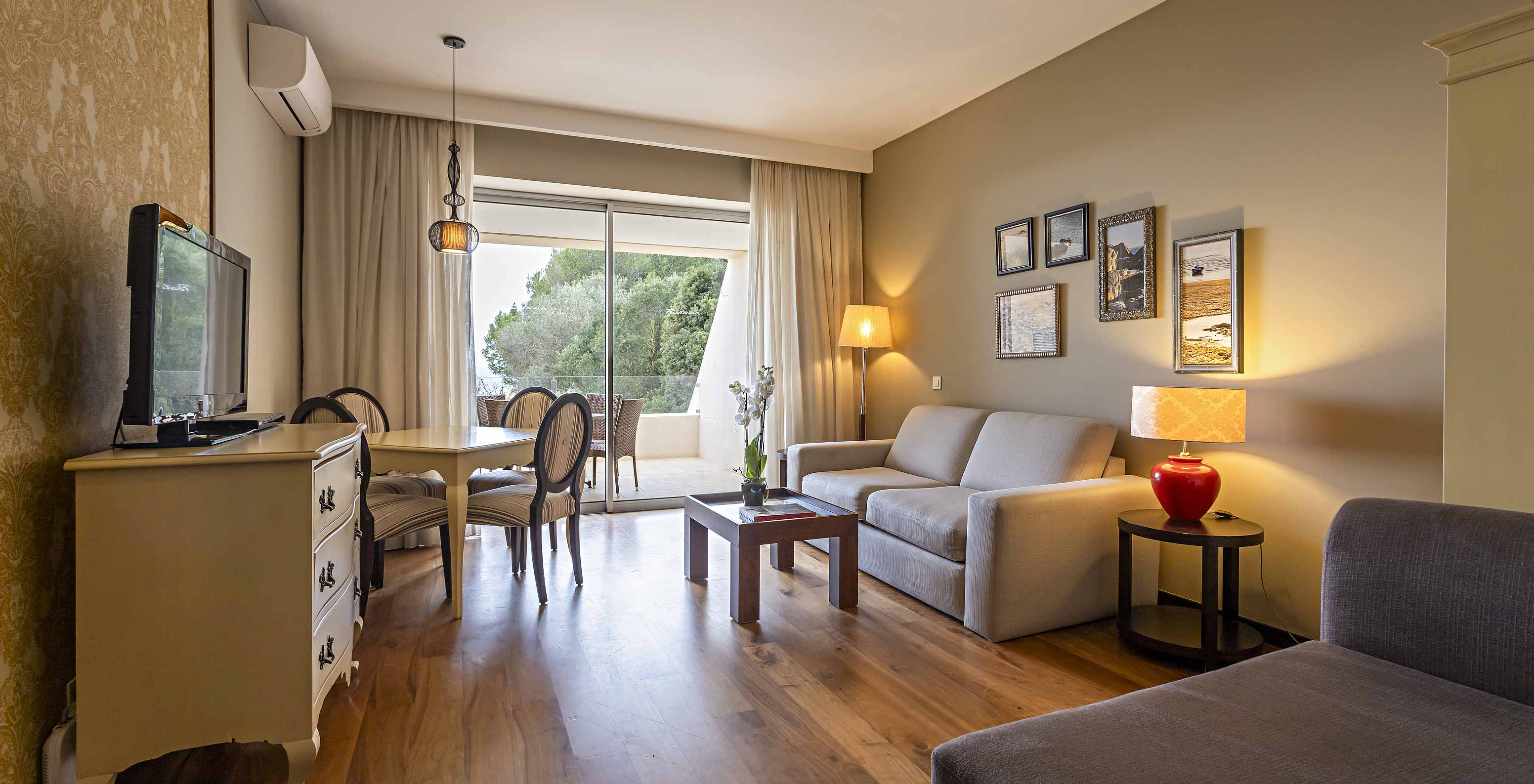 La suite Cliff T1 du Pestana Alvor Praia a un salon avec 2 canapés, une commode avec TV, une table à manger et des chaises