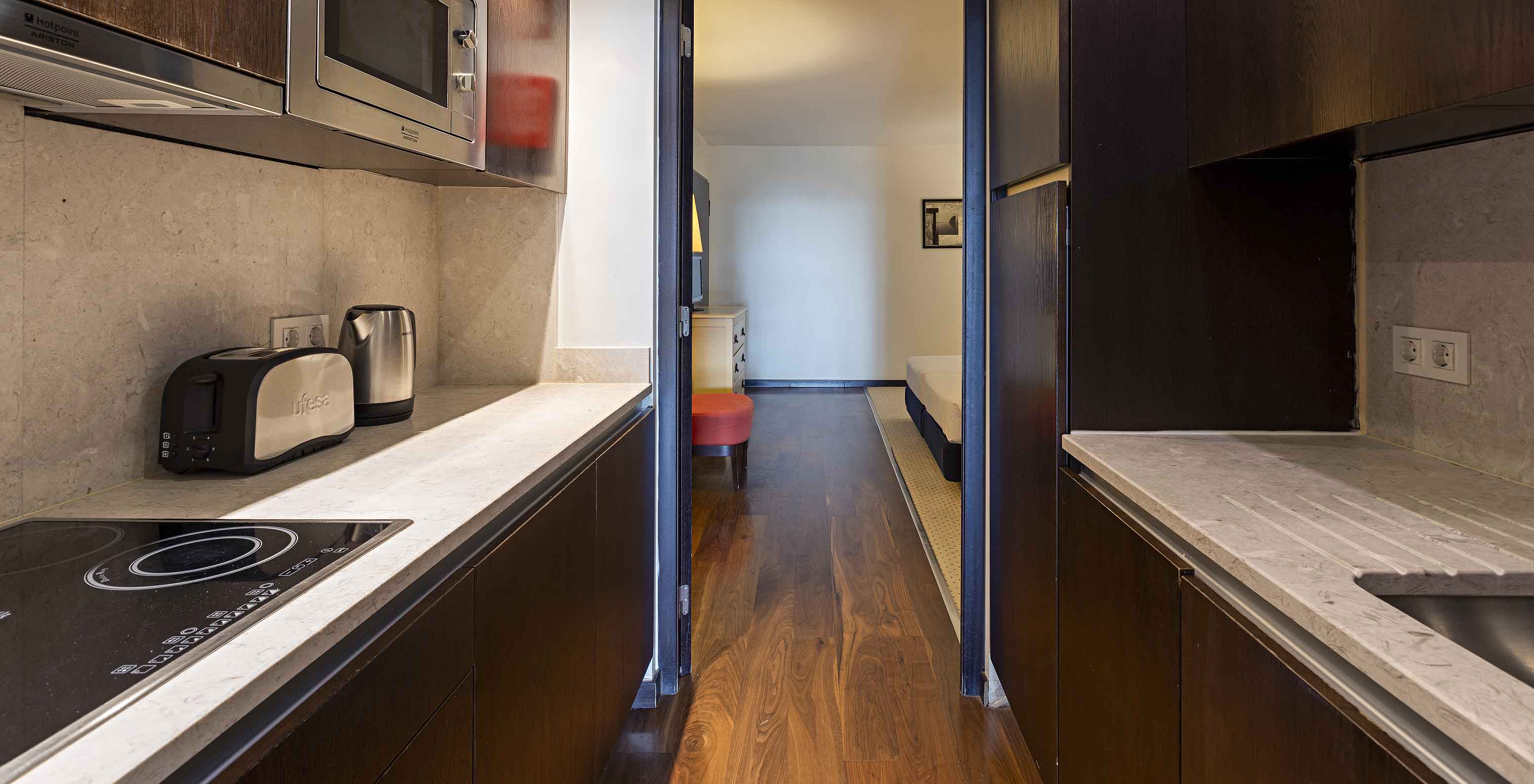 La suite Cliff T2 du Pestana Alvor Praia a une cuisine équipée en bois foncé et pierre, avec cuisinière et micro-ondes