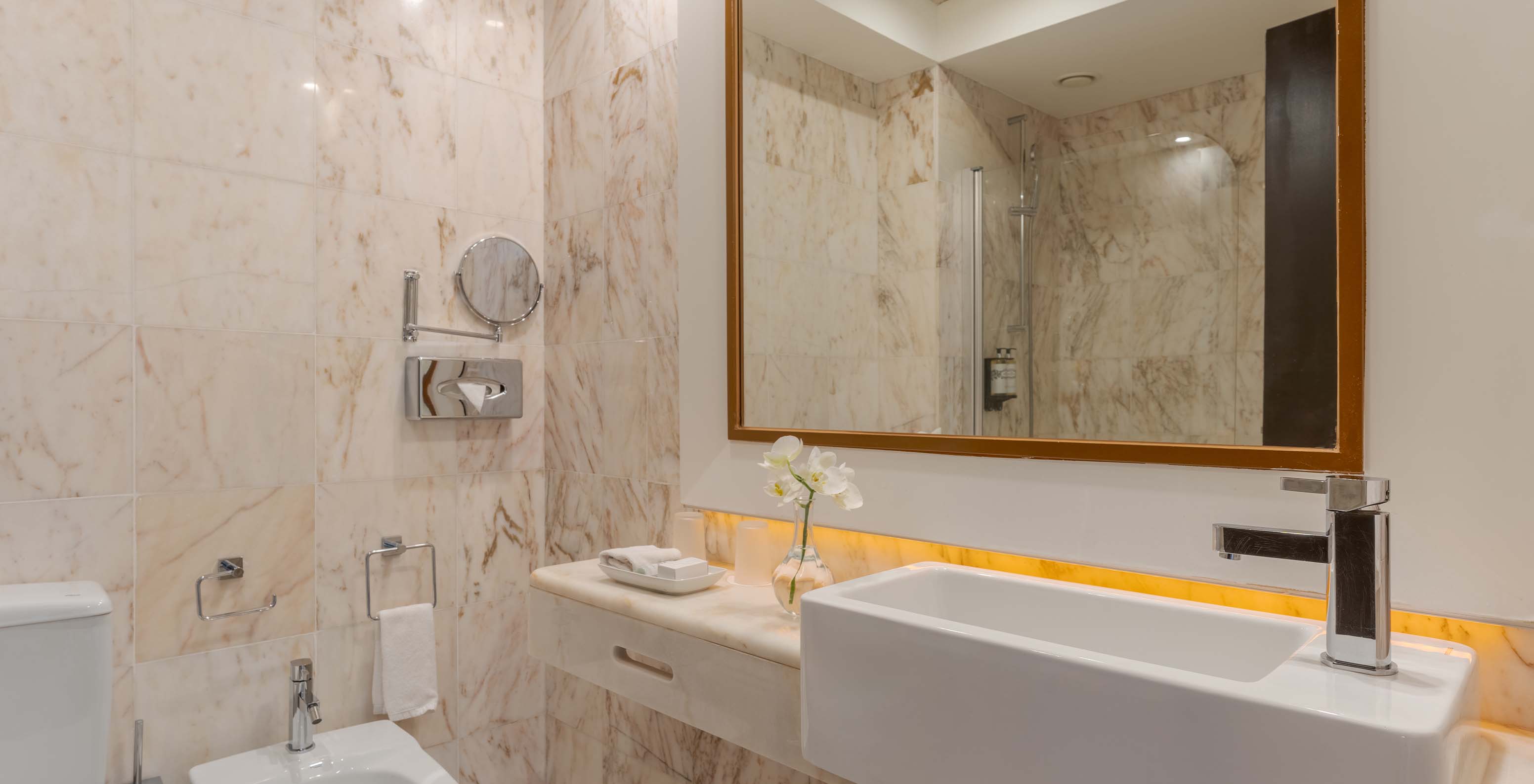 La Suite Vue Jardin du Pestana Alvor Praia a salle de bain en marbre avec bidet, lavabo, miroirs et vase avec fleur