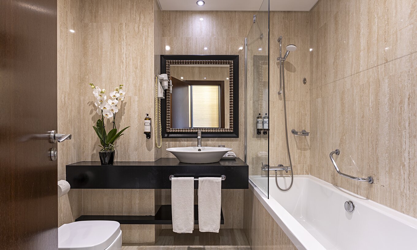 La suite Cliff T2 du Pestana Alvor Praia a une salle de bain moderne avec baignoire, lavabo, toilettes, miroir et fleurs