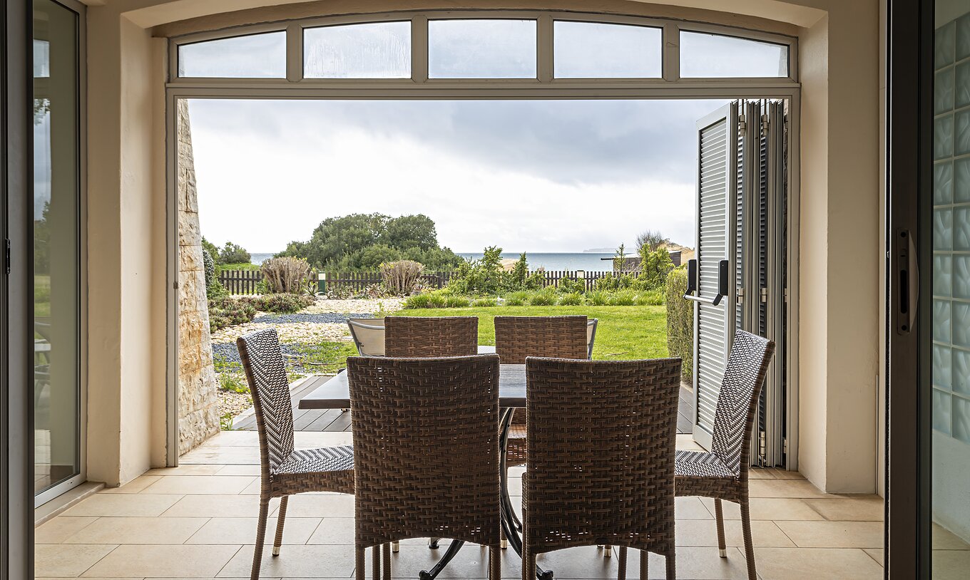 La suite Cliff T2 du Pestana Alvor Praia a un porche avec table, chaises et un jardin avec vue sur la plage
