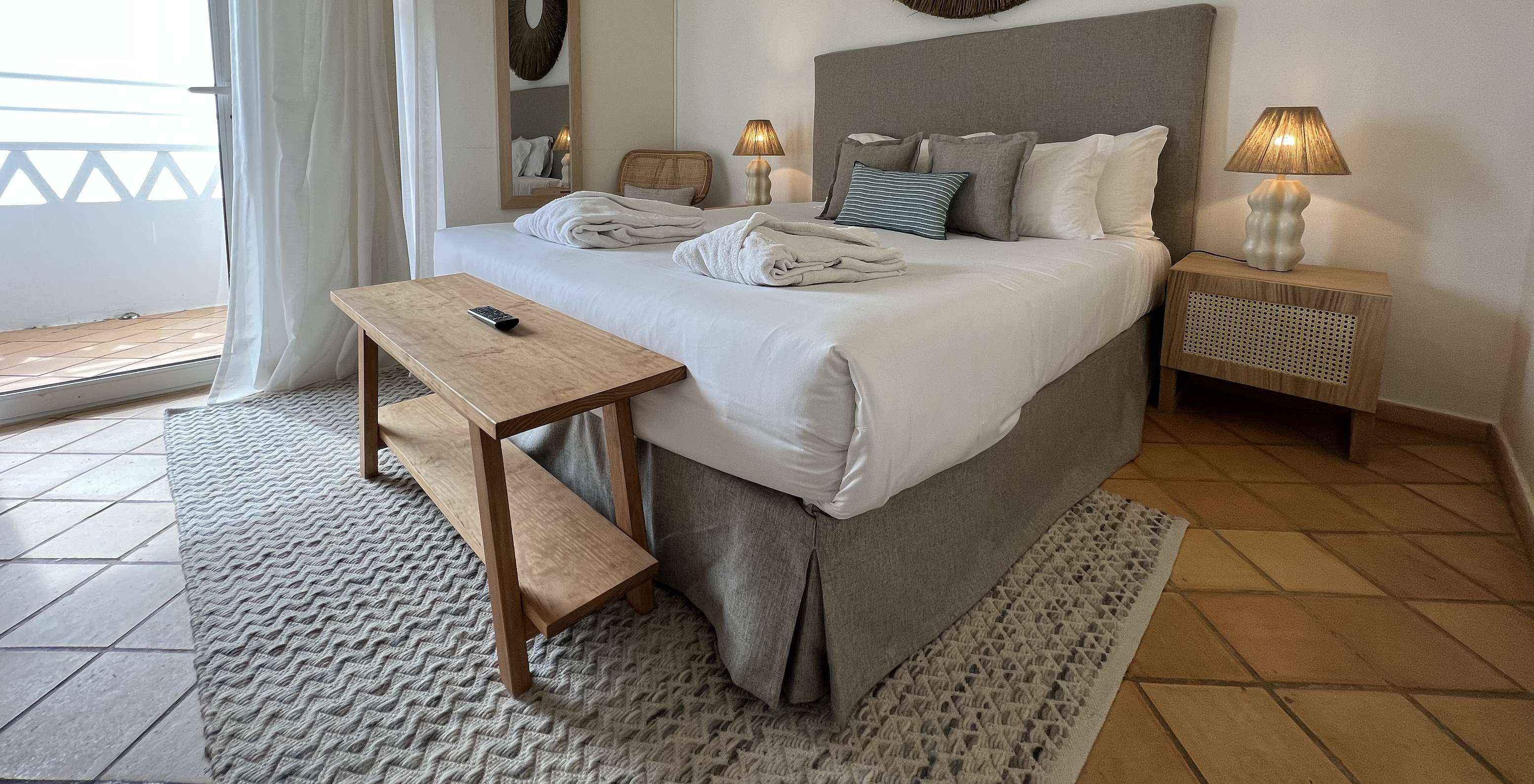 L'Appartement T2 Premium du Pestana Palm Gardens a un lit avec deux peignoirs, coussins et une fenêtre avec balcon