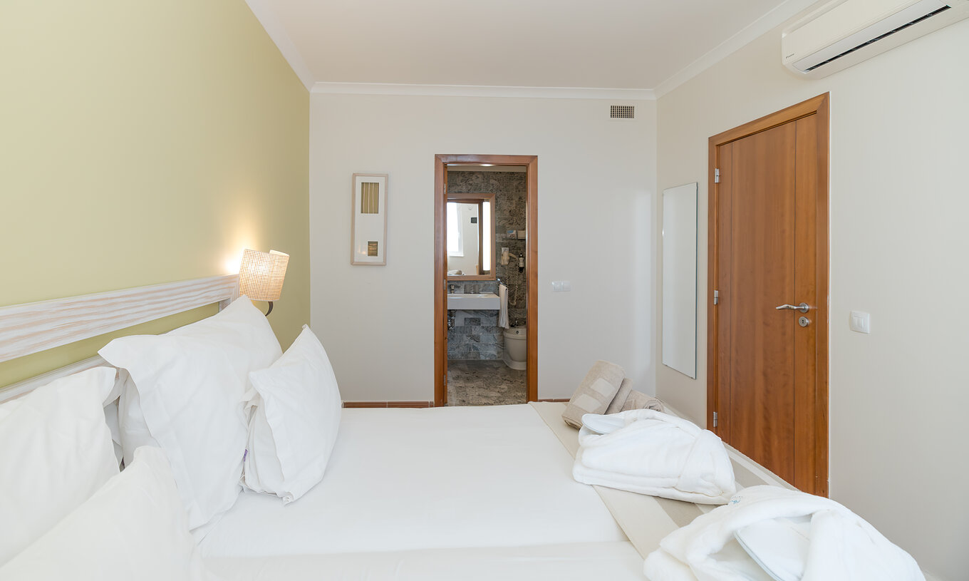 La Suite Vue Mer du Pestana Viking a deux lits avec table de chevet et une salle de bain