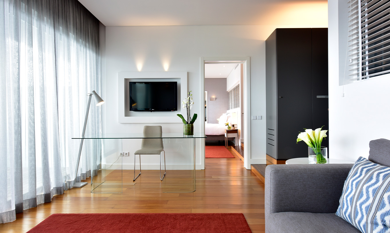 La Suite du Pestana Cidadela Cascais a un salon avec canapé gris, télévision, bureau et une fenêtre confortable