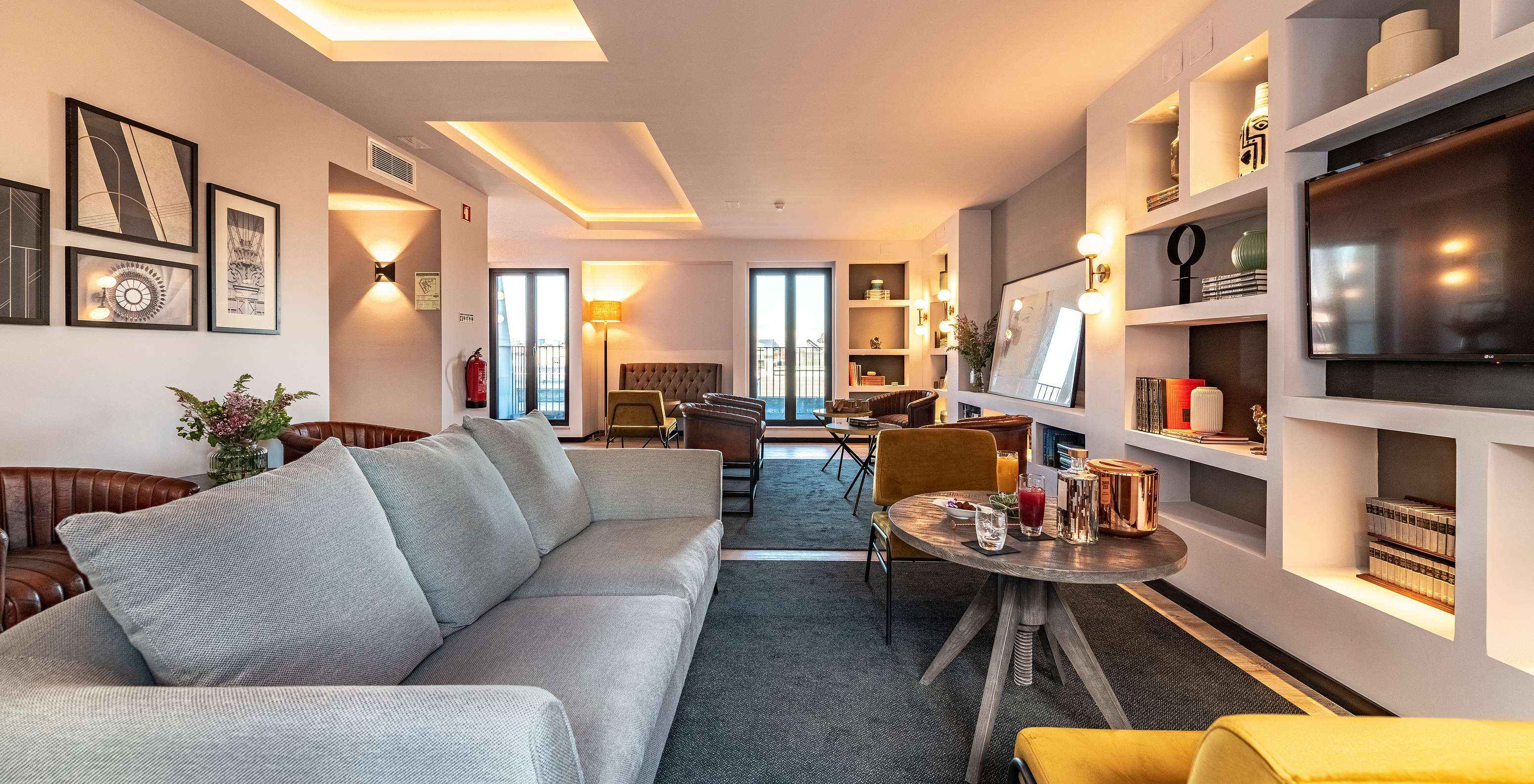 Lounge avec canapés chaises tables tableaux télévision tapis et objets de décoration avec fenêtres donnant sur la ville