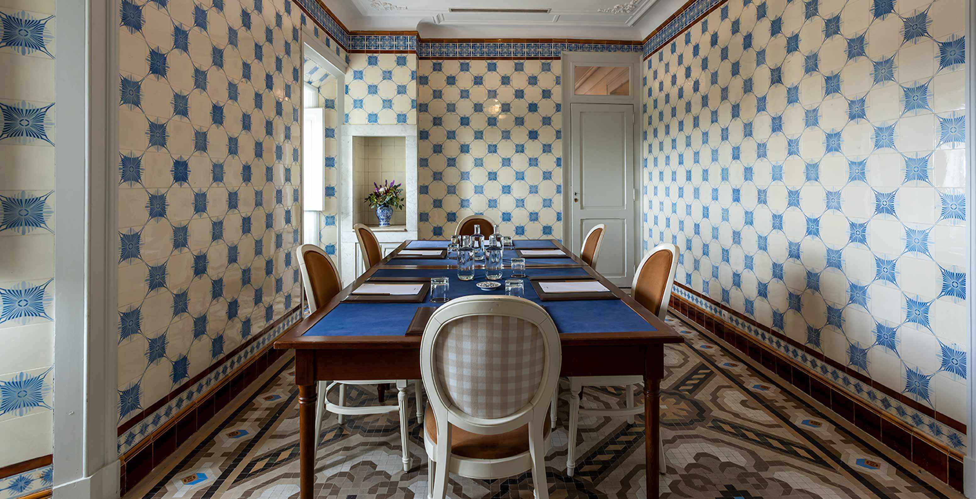 Le Pestana Palace Lisboa a une salle de réunion avec azulejos bleus et blancs et table entourée de chaises blanches