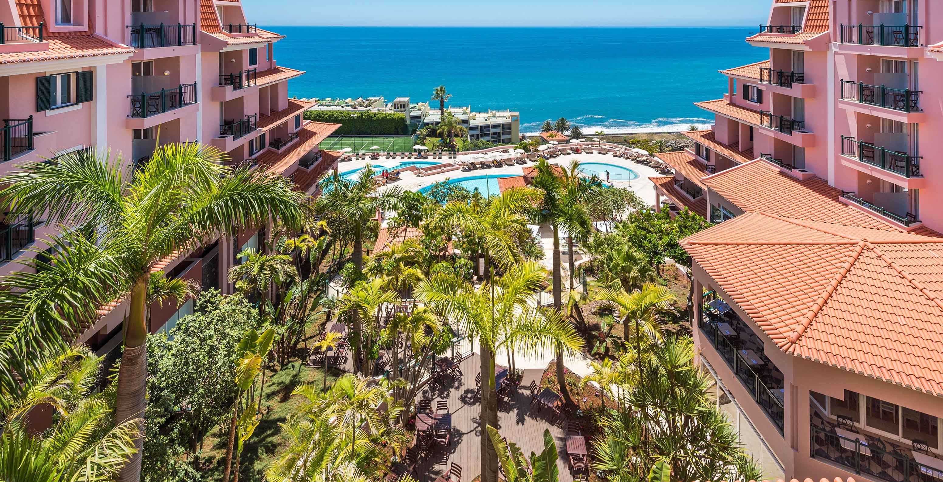 Vue du Pestana Royal All Inclusive, avec des bâtiments roses, une piscine et l'océan en arrière-plan