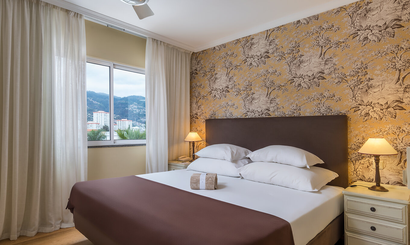 Le Supérieur Famille du Pestana Village a un lit double avec tête de lit et couvre-lit marron, papier peint floral et balcon