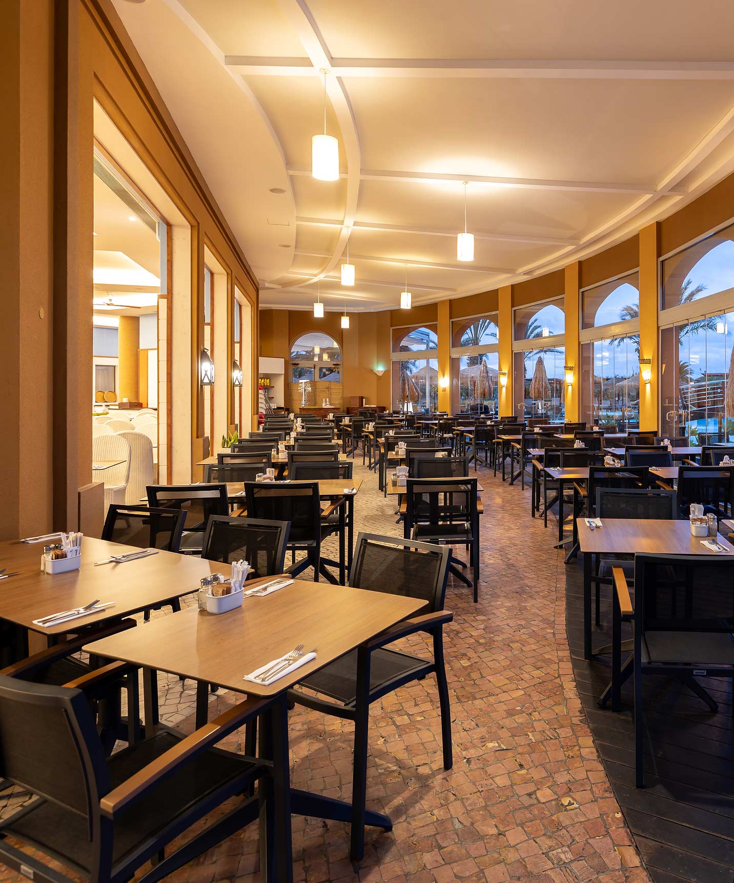 Salle à manger informelle du Pestana Porto Santo All Inclusive avec plusieurs tables carrées et chaises