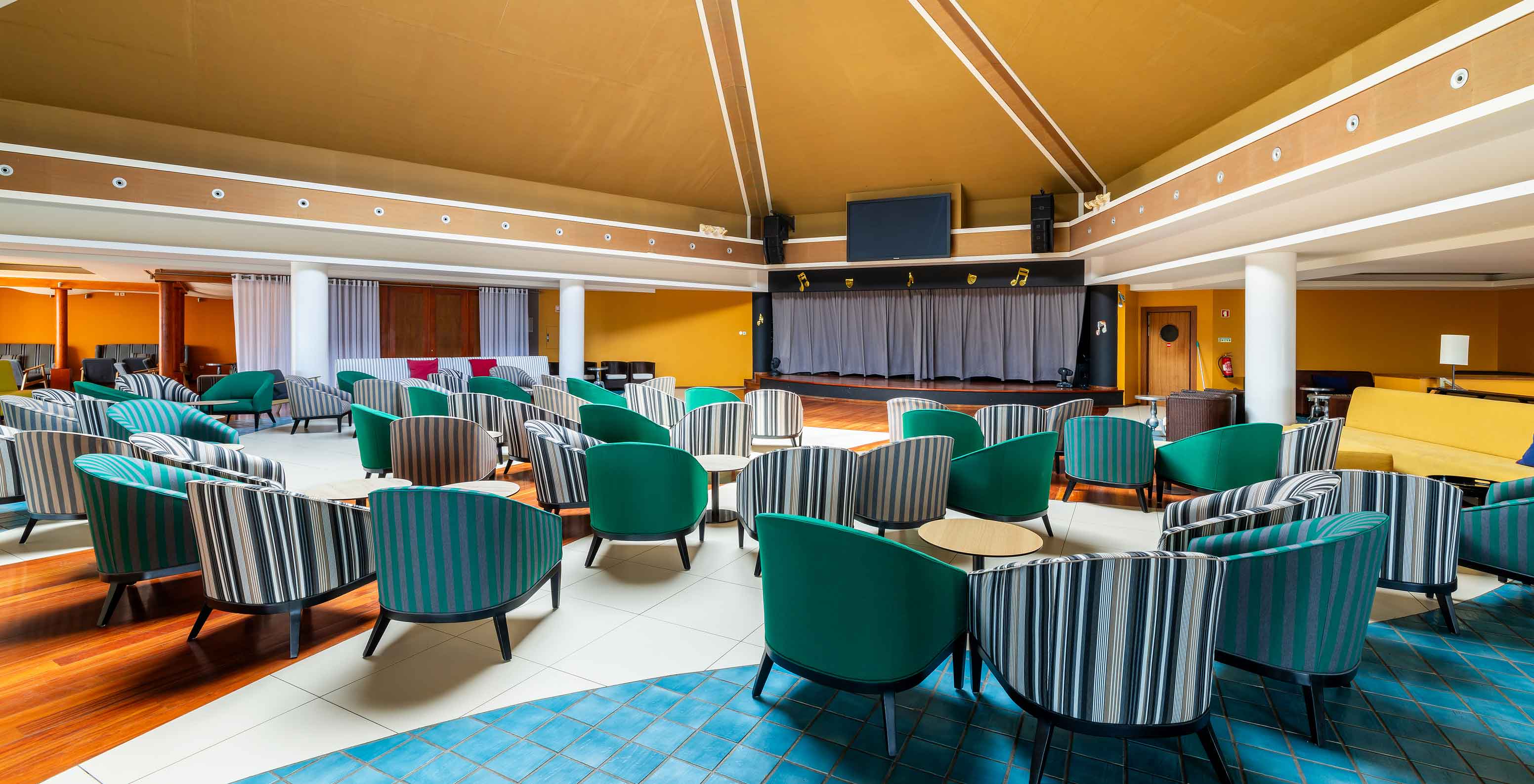 Le bar Sunset du Resort 5 étoiles à Porto Santo dispose d’un grand espace avec des murs jaunes et des chaises vertes.