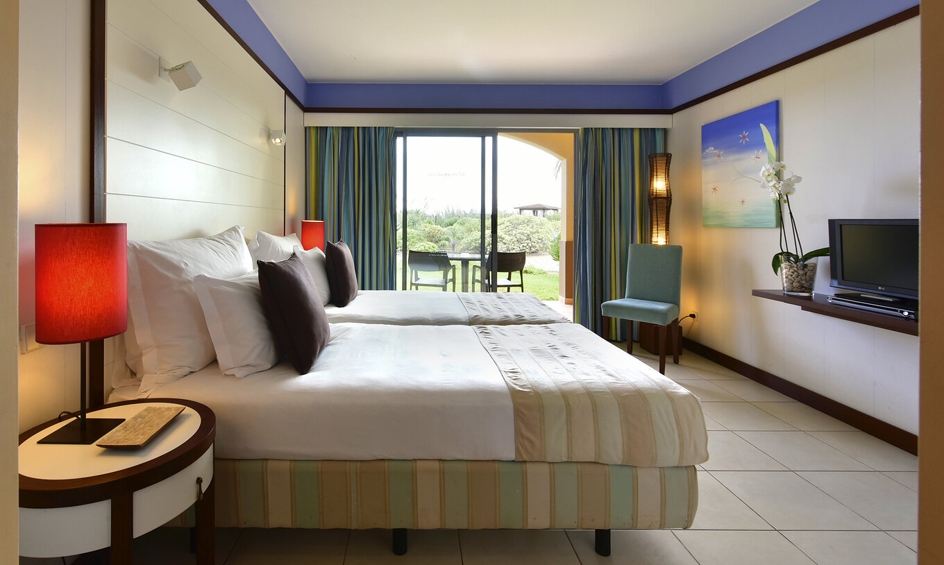 Le Double Classique du Pestana Porto Santo All Inclusive a deux lits, une chaise et un balcon avec table et vue jardin