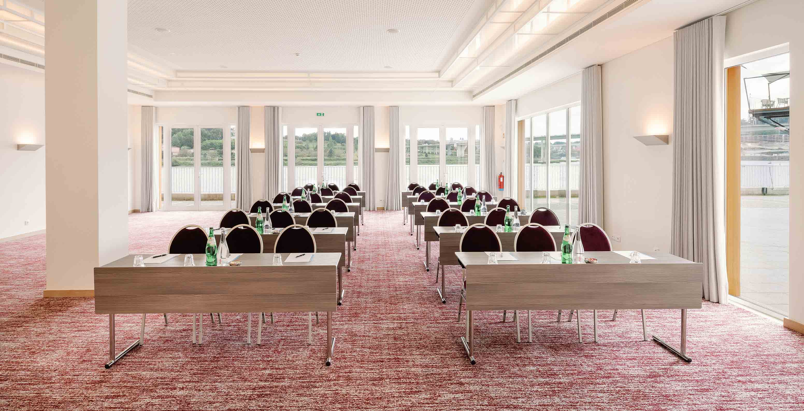 Salle Douro V avec tables chaises et grandes fenêtres à l’hôtel Pestana Douro Riverside avec piscine face au Douro