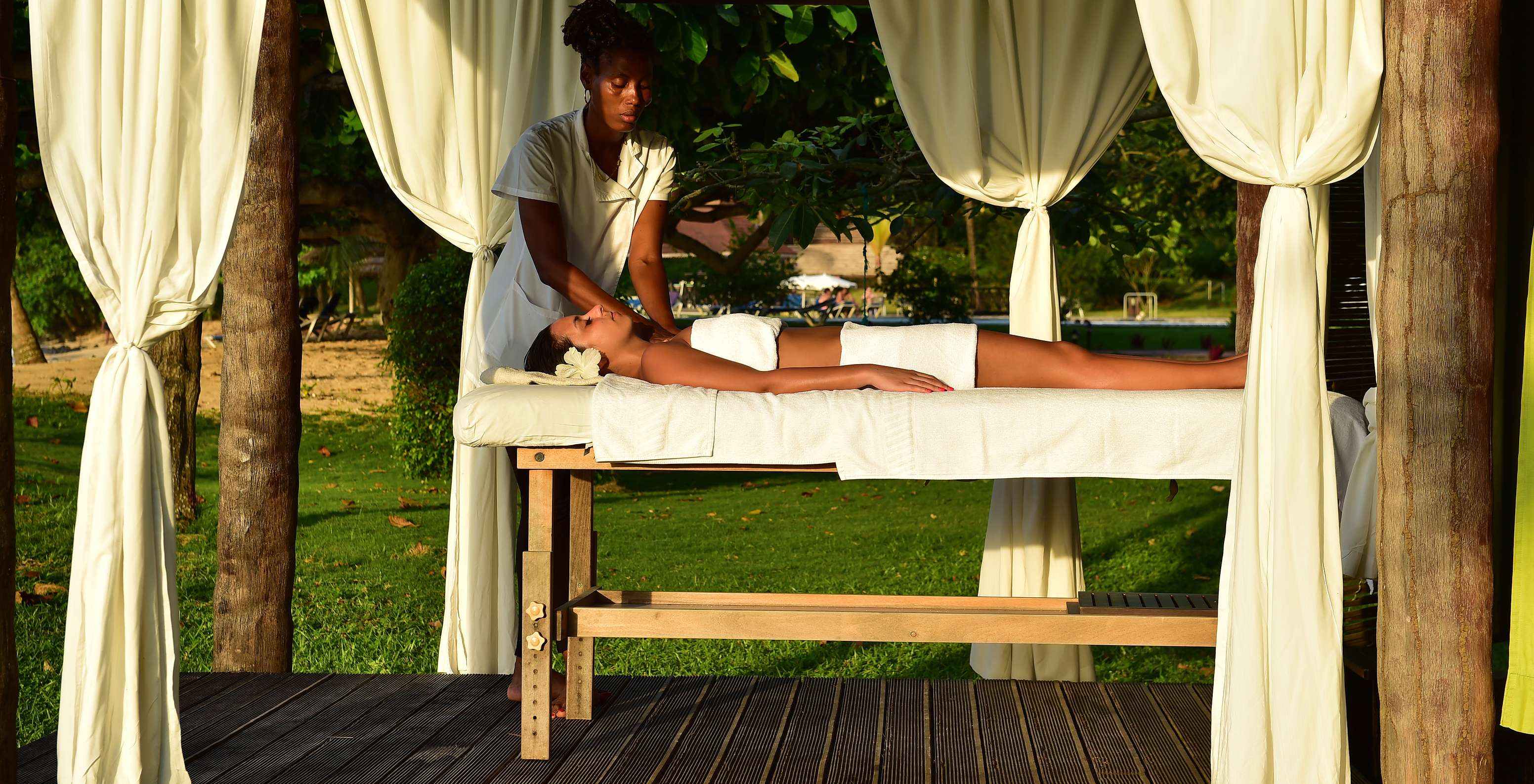 Fille avec une fleur dans les cheveux recevant un massage en plein air à l'hôtel pour vacances, avec piscine et spa