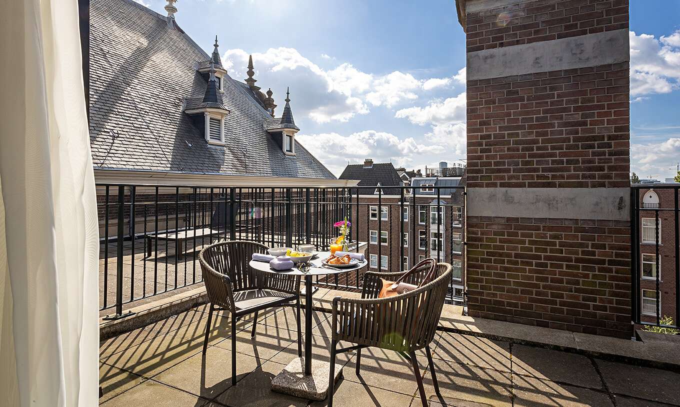 La chambre Executive Terrace du Pestana Amsterdam Riverside a un balcon, avec une table avec nourriture et deux chaises