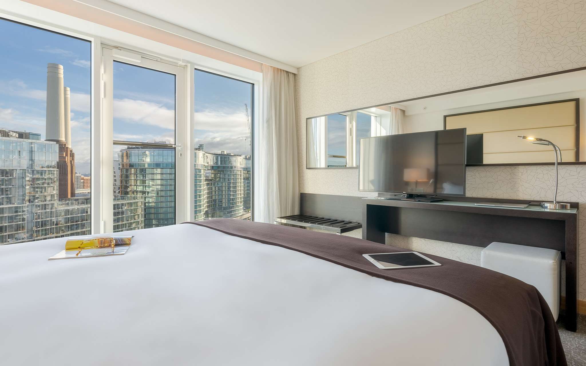 Chambre avec lit double, télévision, miroir et grandes fenêtres donnant sur la ville de Londres