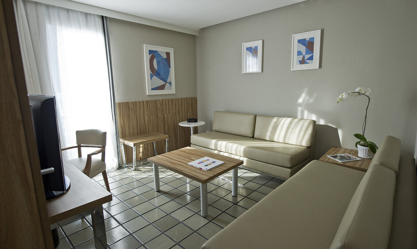 De Standaard Suite van Pestana Rio Atlântica heeft een woonkamer met twee comfortabele beige banken, een salontafel en televisie