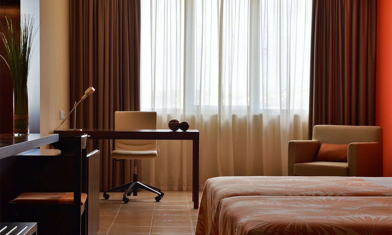 De standaardkamer van Pestana Tropico heeft een bureau met lamp en stoel, en een fauteuil