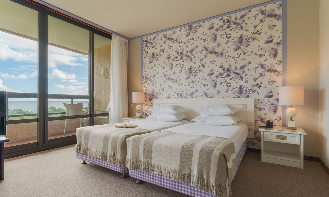 In Junior Suite Tuinzicht van Pestana Bahia Praia staan de bedden naast het balkon met uitzicht op tuinen en zee