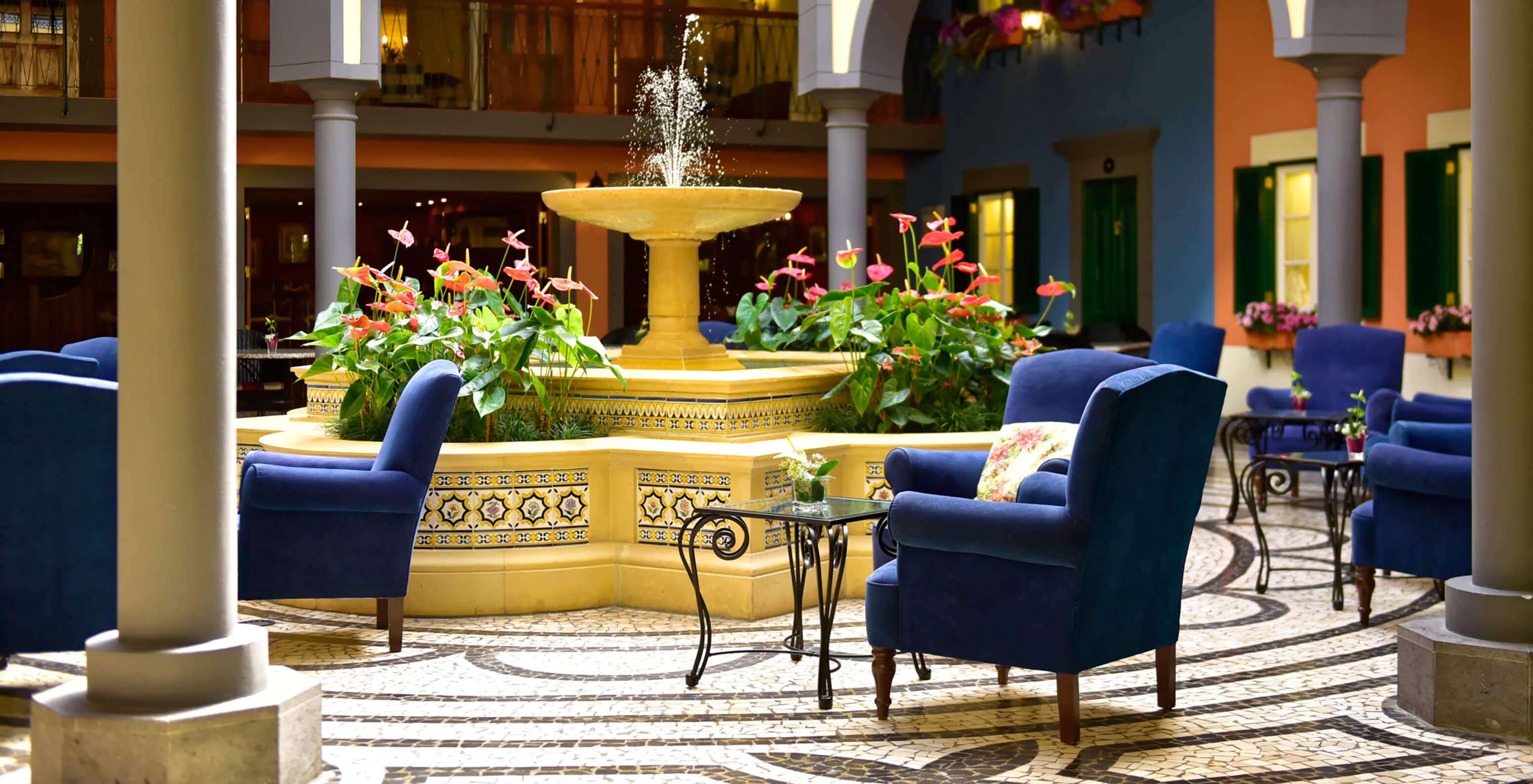 Binnenplaats met centrale fontein, roze bloemen, blauwe stoelen bij Pestana Village, Hotel met Zwembad in Funchal