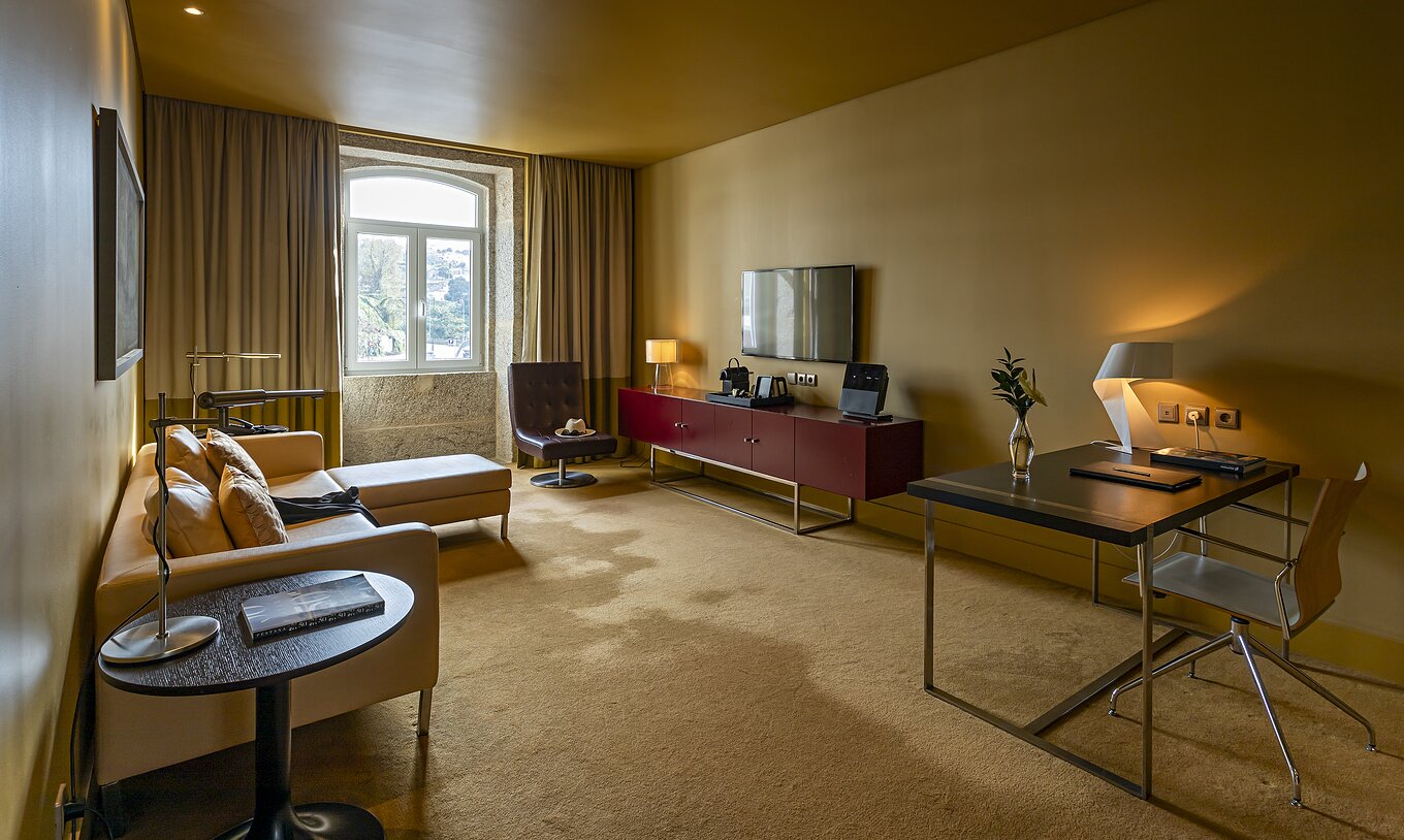 De Junior Suite heeft een kamer met chaise-longue bank, een bureau en een TV