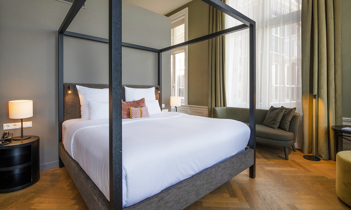 Junior Suite - River View van Pestana Amsterdam Riverside heeft tweepersoonsbed met hemelbed en groene bank