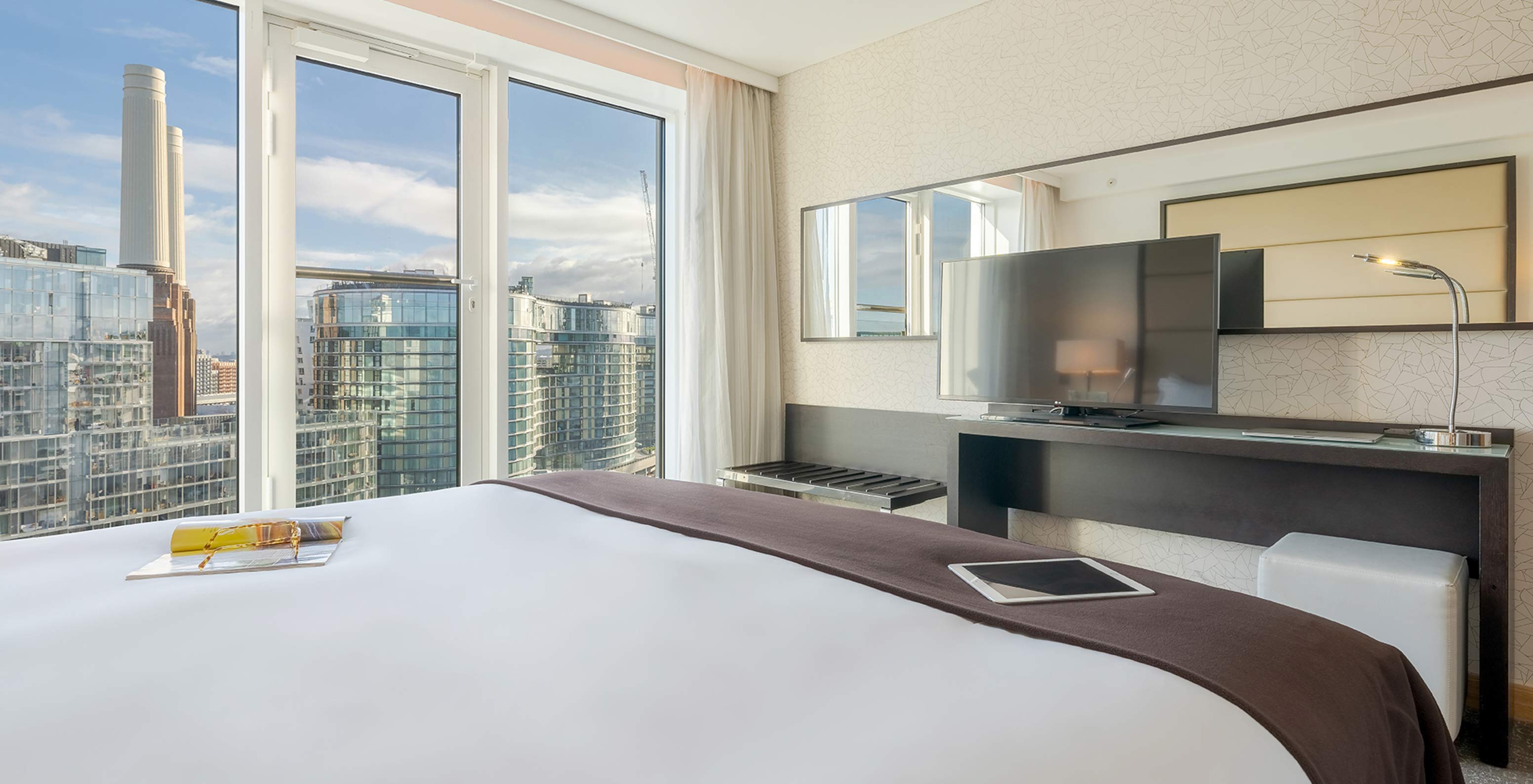 De Superior King van Pestana Chelsea Bridge heeft bed, bureau met tv, bank en ramen met uitzicht op de stad