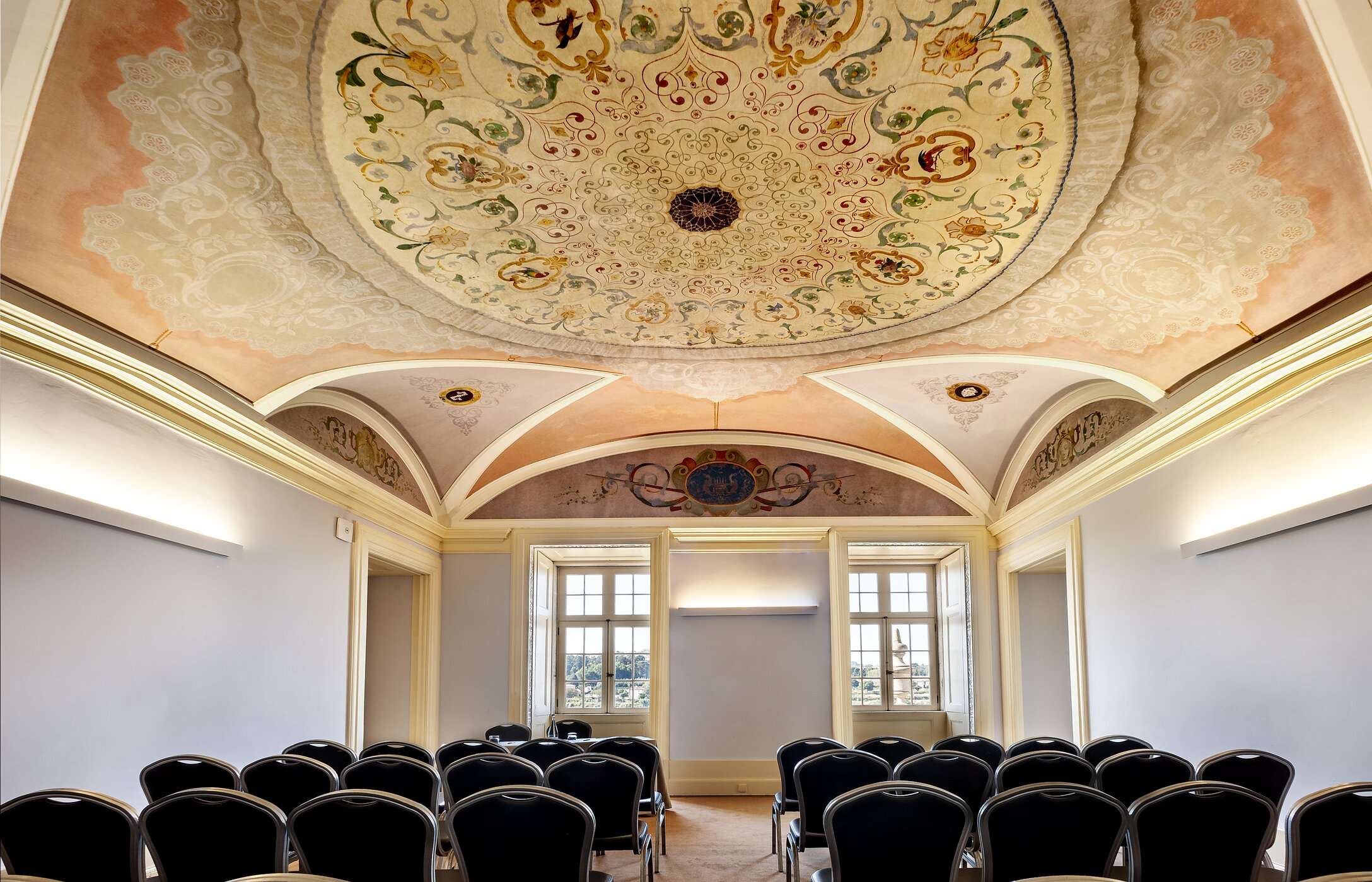 Vergader- of conferentieruimte, met plafond met details, stoelen en grote ramen die natuurlijk licht binnenlaten