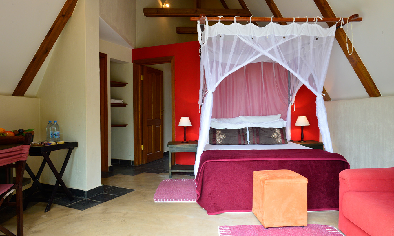 O Bungalow T1 do Pestana Bazaruto Lodge tem uma decoração em tons de vermelho com cama de casal, sofá e secretária