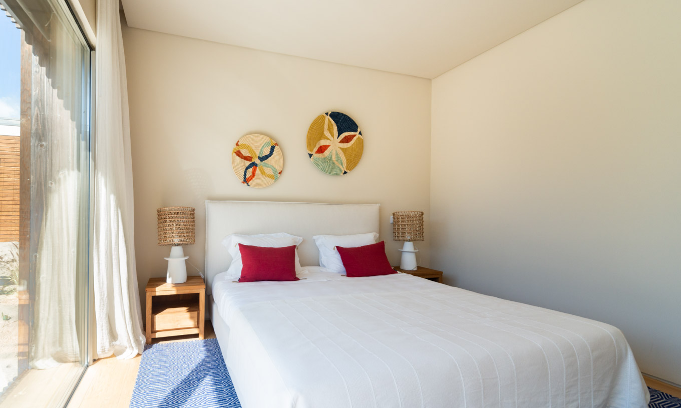 A Villa exclusiva com piscina do Pestana Tróia Eco Resort tem um quarto com cama de casal, almofadas vermelhas e tapete azul