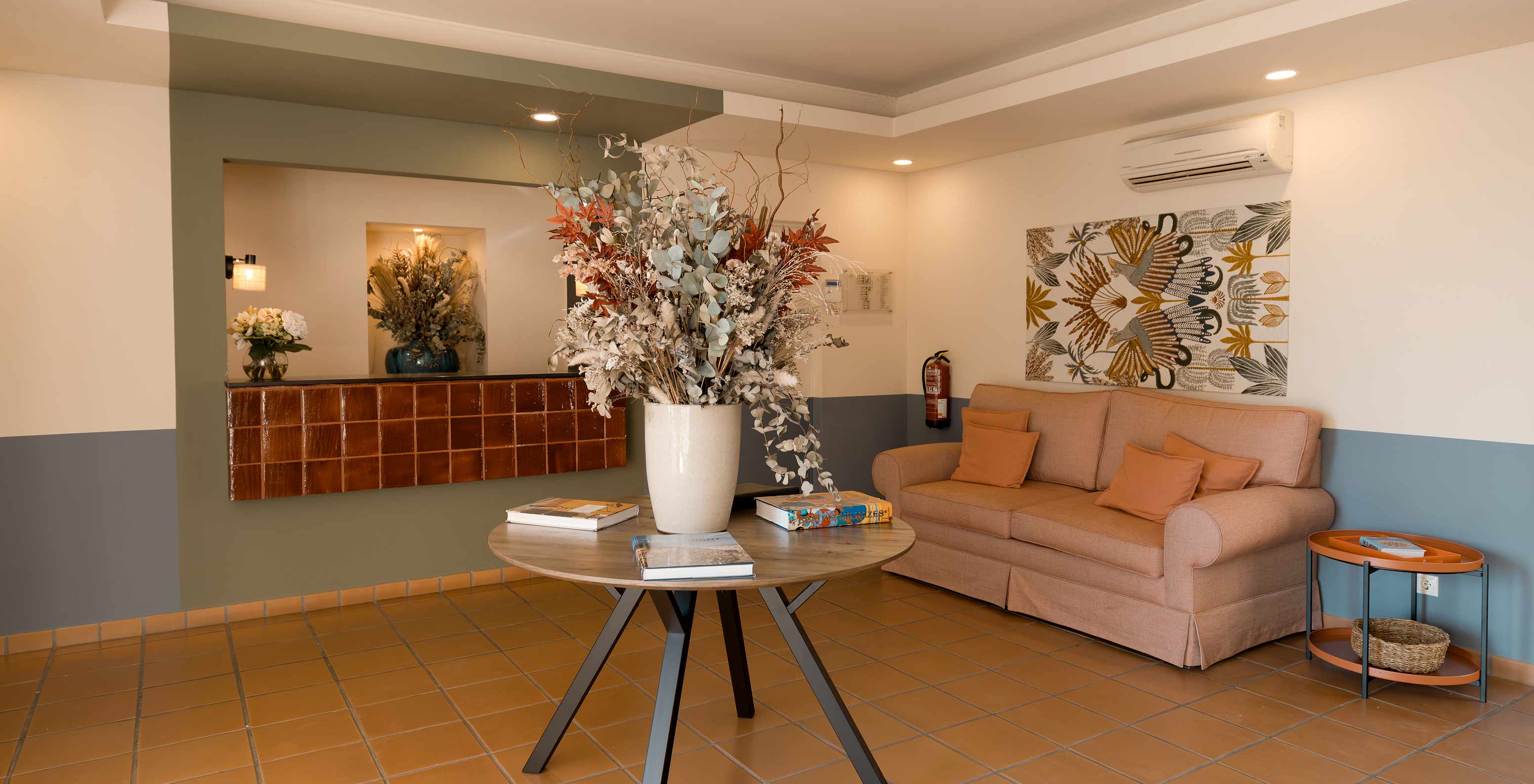 Receção do Hotel Perto da Praia com Piscina, com um sofá laranja confortável e uma mesa de apoio com um jarro de flores