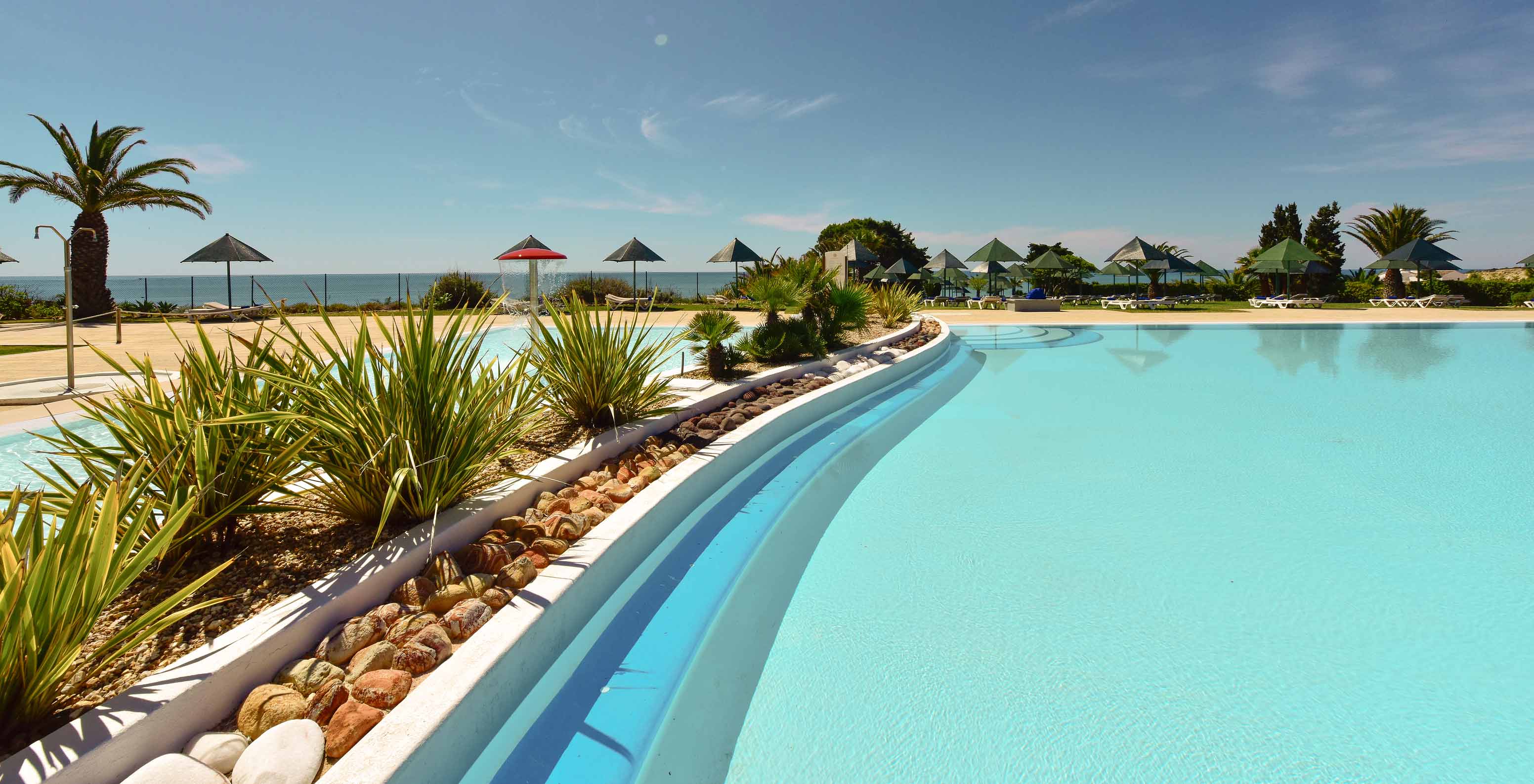 Piscina exterior do Pestana Viking, rodeada de vegetação, com várias espreguiçadeiras e vista para o mar