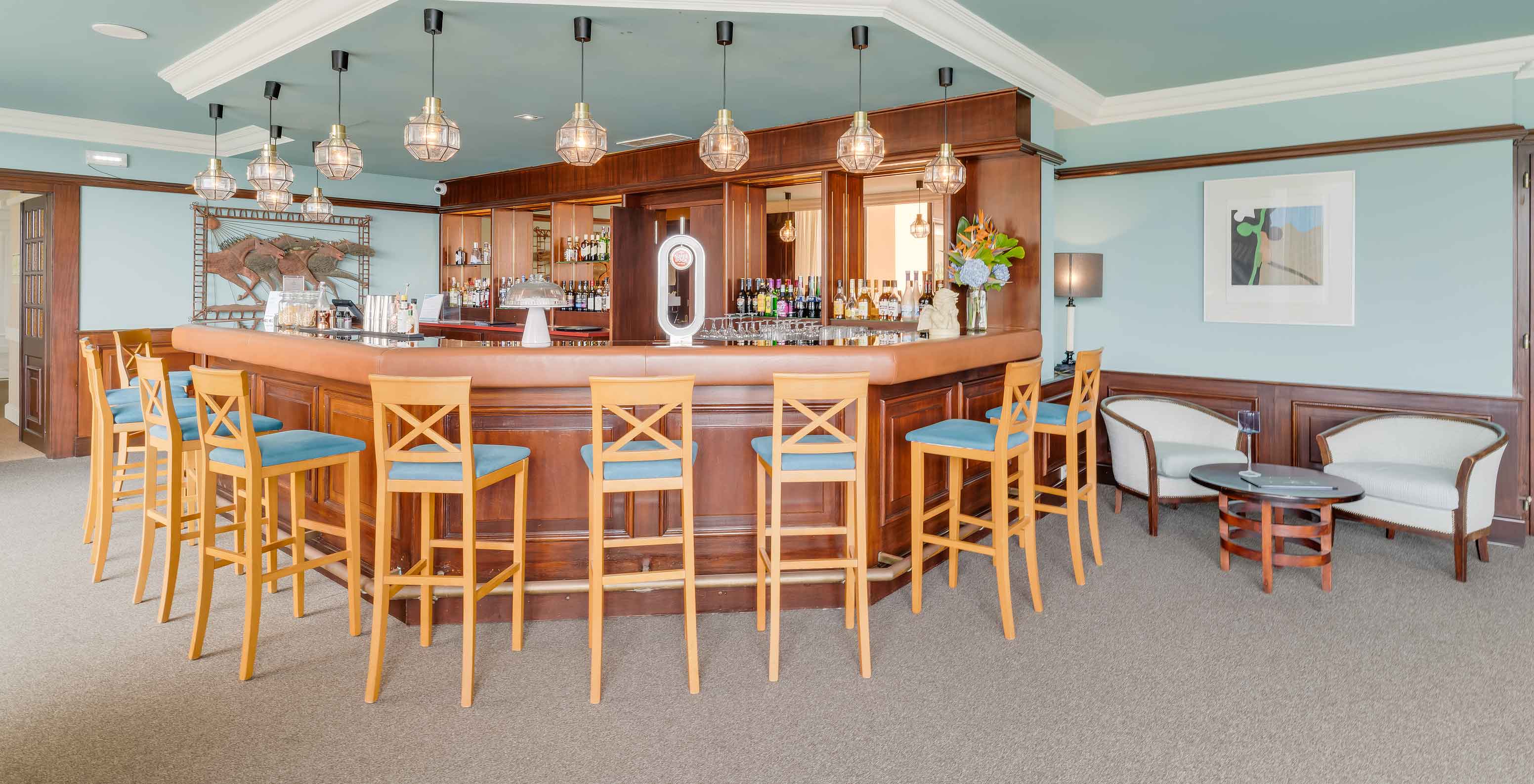 Bar do Pestana Bahia Praia com cadeiras altas, balcão em madeira e iluminação moderna com lâmpadas pendentes