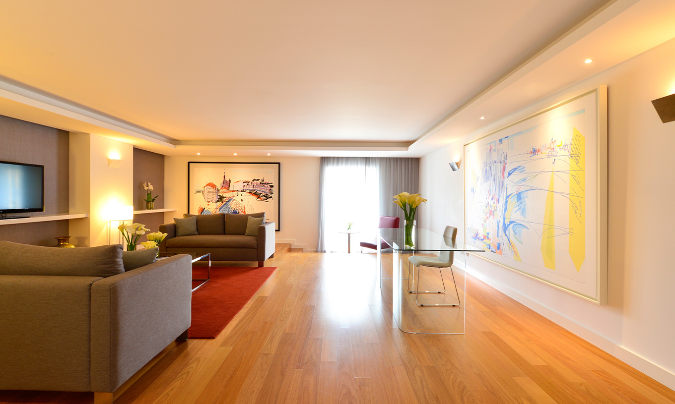 A Suite Presidencial do Pestana Cidadela Cascais tem uma sala com uma secretária transparente e cadeira, quadros e um sofá