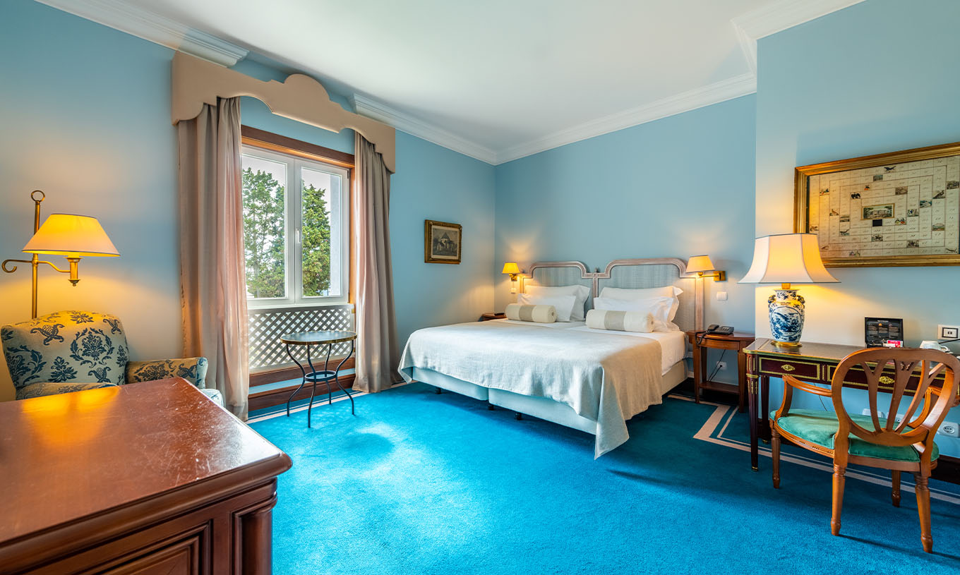 O Deluxe do Pestana Palace Lisboa tem duas camas individuais, uma janela, poltrona, secretária e uma carpete azul