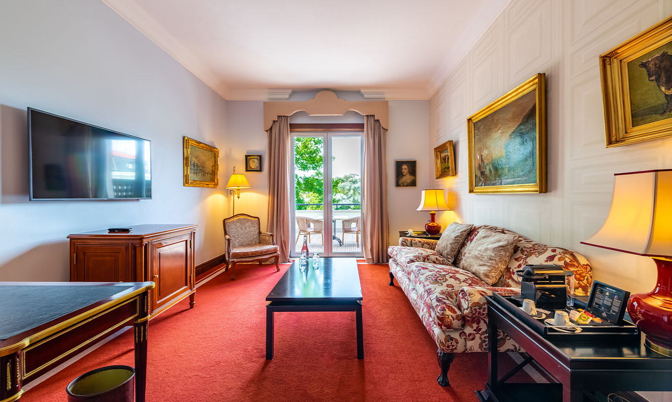 A Suite Collection do Pestana Palace Lisboa tem uma sala com sofá, televisão, janela com acesso à varanda e quadros na parede
