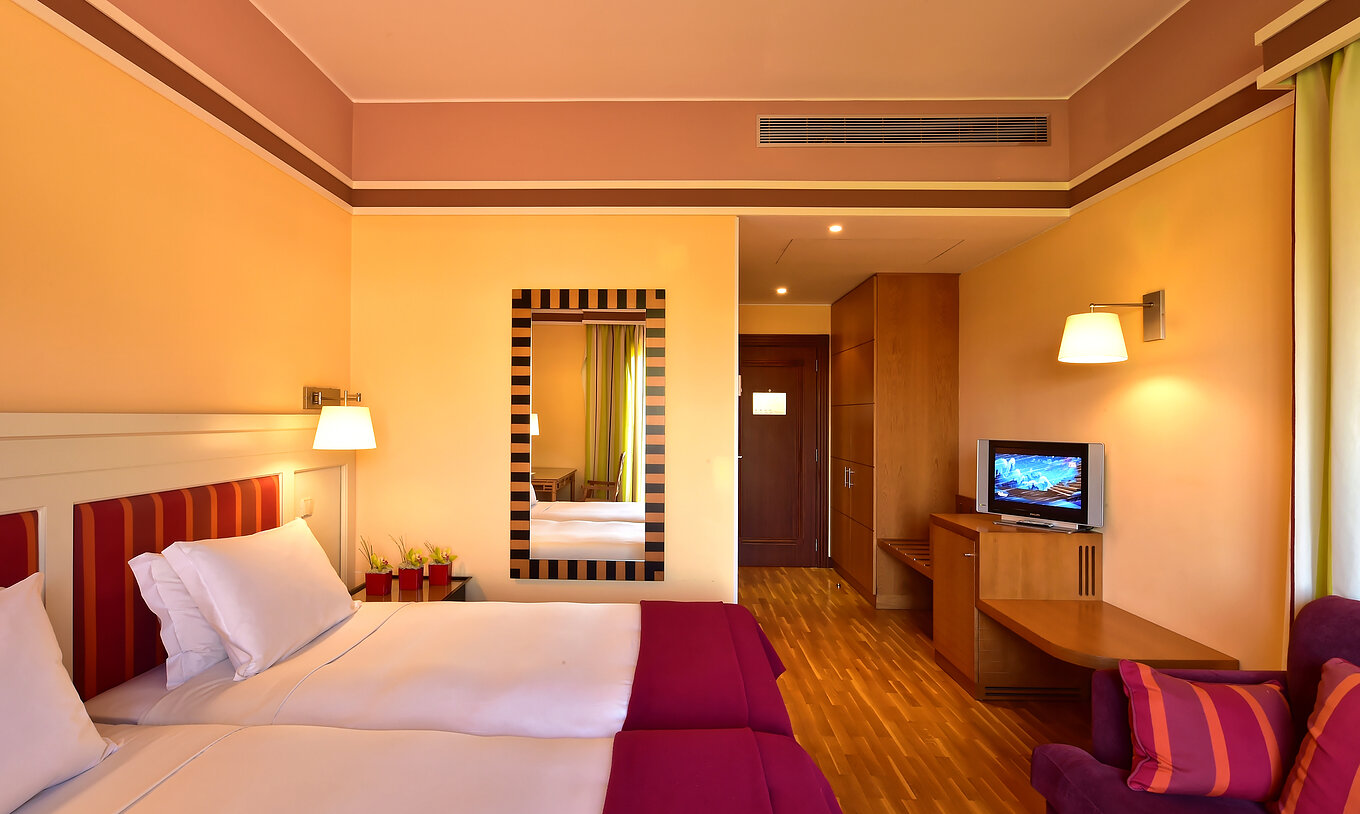 O Duplo Clássico - Vista Jardim do Pestana Sintra Golf tem duas camas, um espelho na parede, uma televisão e um sofá