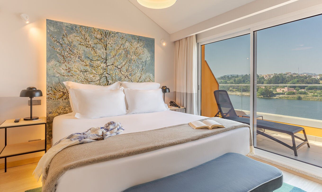 A Suite do Pestana Douro Riverside conta com uma cama de casal, varanda com vista, mesa de cabeceira com candeeiro e telefone