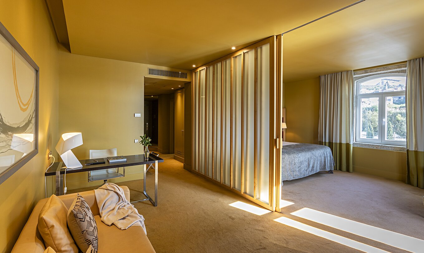 A Standard Suite do Pestana Palácio do Freixo tem uma cama de casal com uma divisória para a sala com sofá e secretária