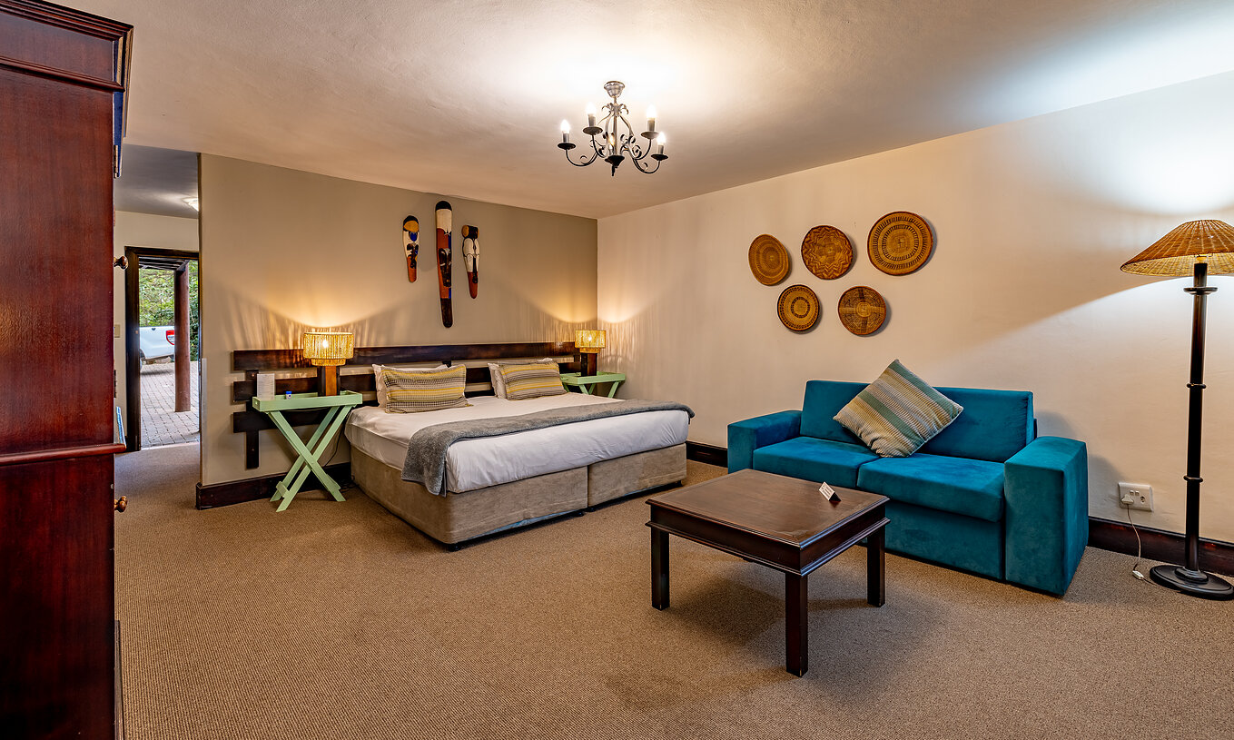 O Premium Room do Pestana Kruger Lodge tem uma cama de casal, um sofá azul e decoração típica africana