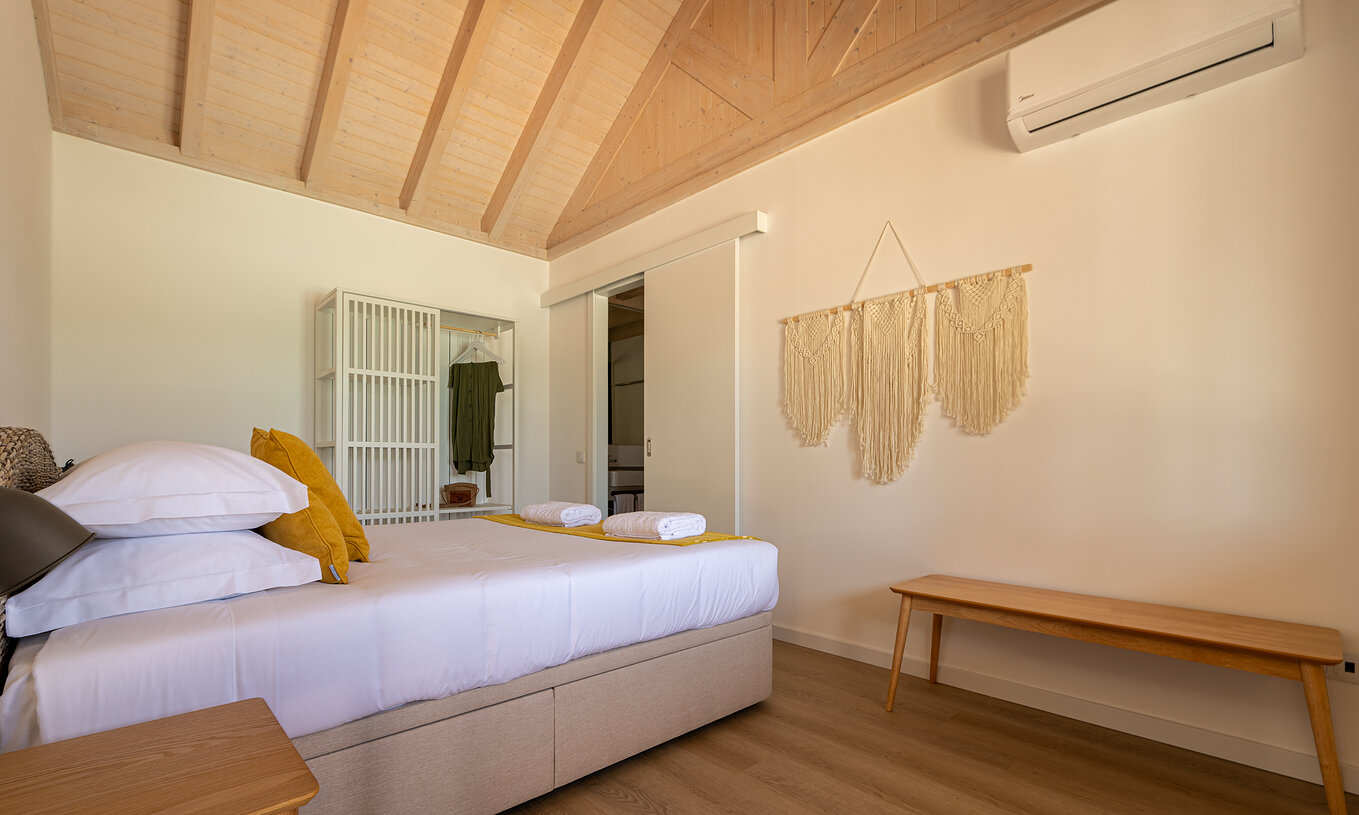 A Standard Green Villa do Pestana Comporta Village Residences tem um quarto minimalista com uma cama e um banco