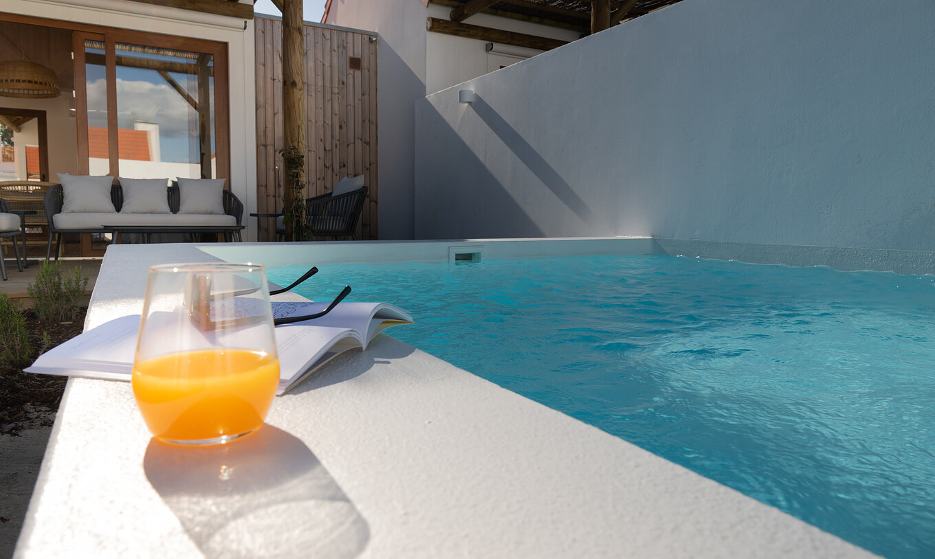 A Superior Green Villa do Pestana Comporta Village Residences tem um pátio com um copo de sumo e um livro perto da piscina