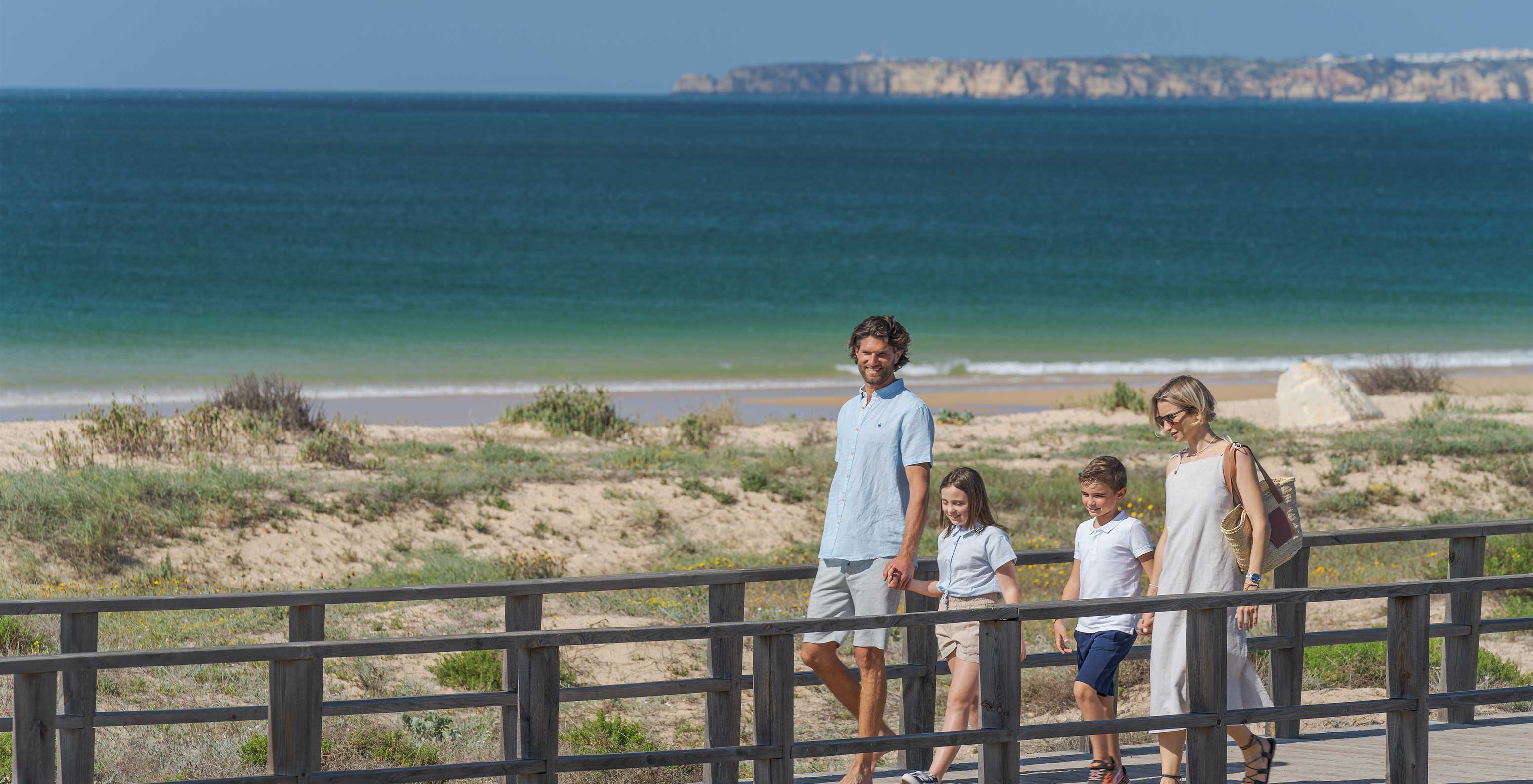 Família passeia sorridente, no passadiço junto à praia do Alvor, no Algarve