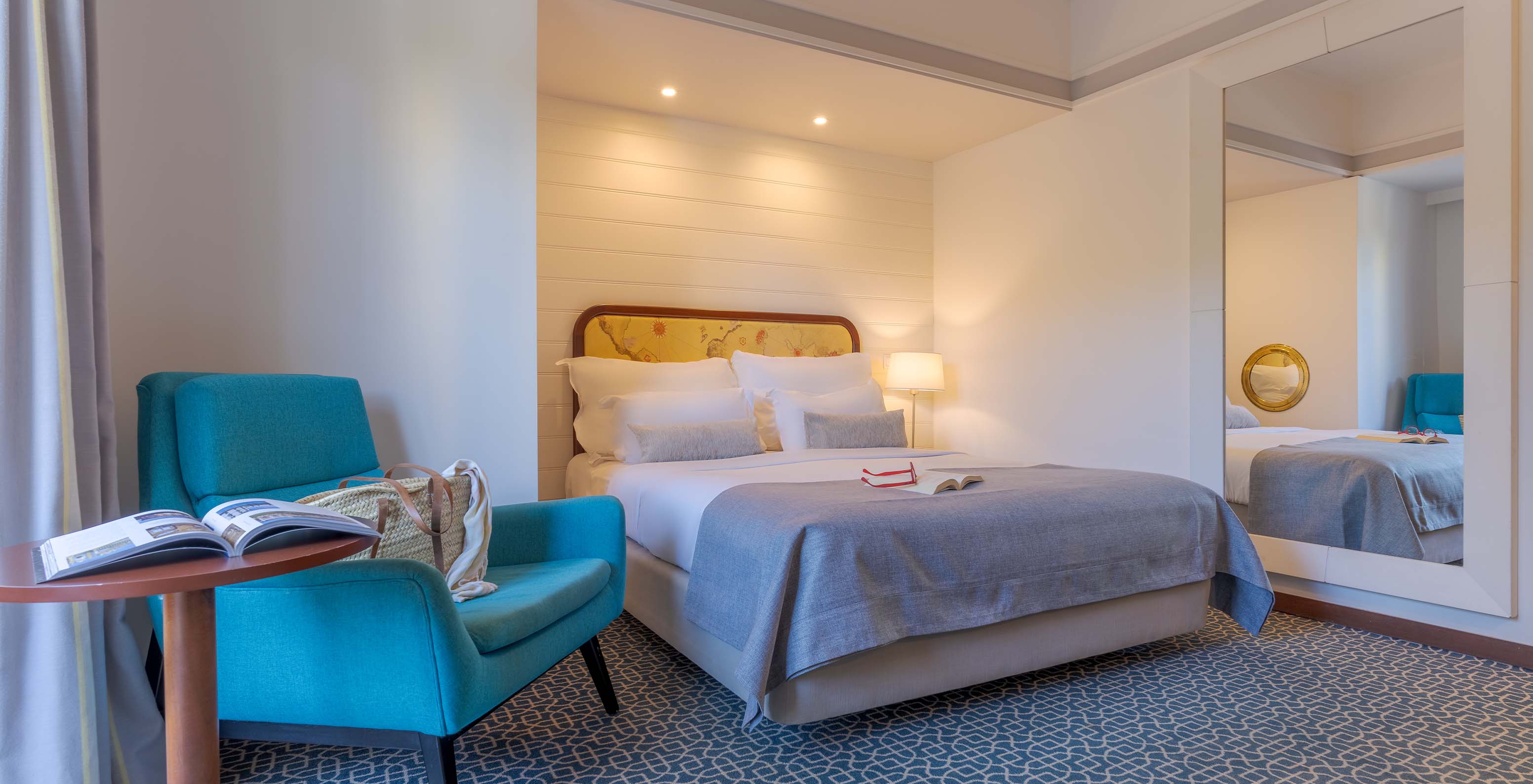 O Deluxe do Pestana Alvor Praia tem uma cama de casal, uma mesa com cadeirão azul, espelho e tapete com padrão geométrico