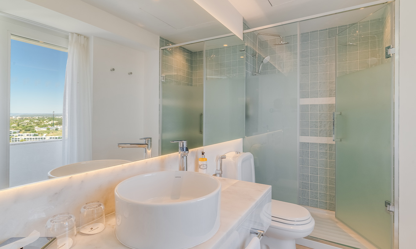 O Quarto Clássico Vista Jardim do Pestana Blue Alvor Beach tem uma casa de banho com lavatório com espelho, sanita e duche